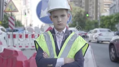 肖像可爱的<strong>小秘密</strong>男孩，穿着商务服，安全设备和建筑工人头盔，站在繁忙的地方